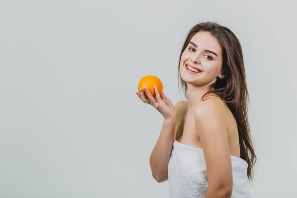 Portrait of a cute young attractive half-woman holding an orange orange on her hands and looking at the camera, isolated over a white background. - Фото, зображення