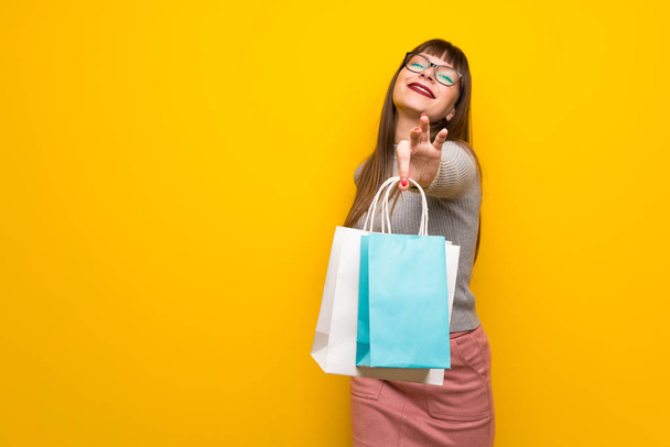 Kobieta w okularach na żółte ściany trzymając sporo torby na zakupy - Zdjęcie, obraz