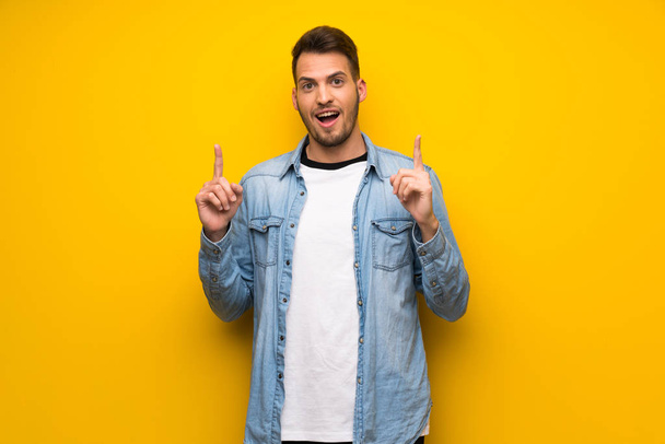 Handsome man over yellow wall pointing with the index finger a great idea - Zdjęcie, obraz