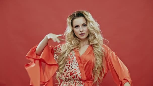 Beautiful young woman in silk robe screaming in excitement after seeing falling stylish clothes while smiling and slowly dancing against red background in front of static camera - slow motion. - Filmmaterial, Video