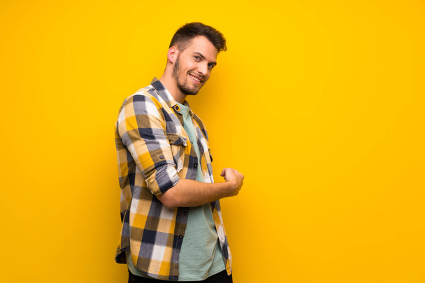 Handsome man over yellow wall pointing back - Photo, Image
