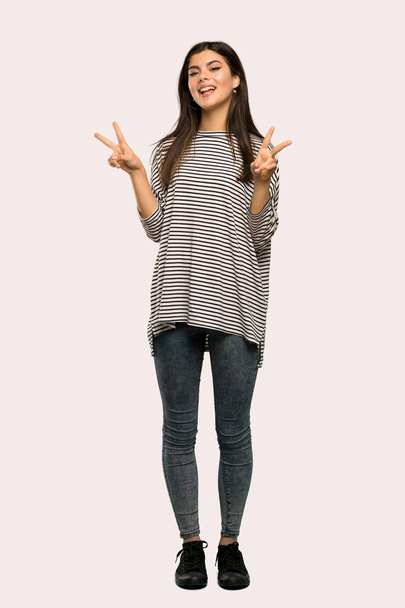 Un plan complet d'une adolescente avec chemise rayée souriante et montrant le signe de la victoire avec les deux mains sur fond isolé
 - Photo, image