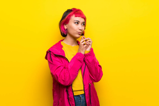 Nuori nainen vaaleanpunaiset hiukset yli keltainen seinä juonittelua jotain
 - Valokuva, kuva
