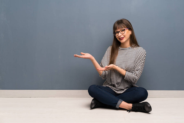 Woman with glasses sitting on the floor extending hands to the side for inviting to come - Photo, Image