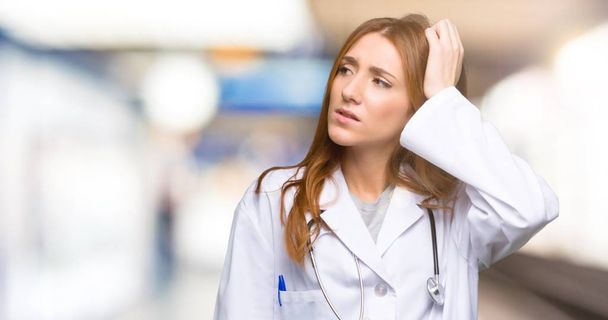 Redhead doctor woman having doubts while scratching head in the hospital - Фото, зображення