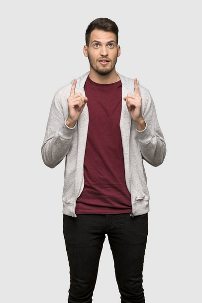 Man with sweatshirt pointing up and surprised over grey background - Zdjęcie, obraz