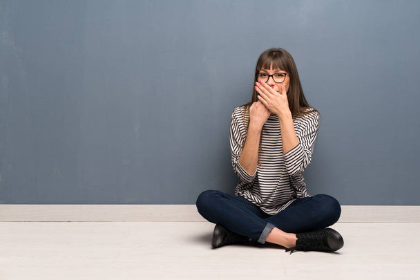 Woman with glasses sitting on the floor covering mouth with hands for saying something inappropriate - Photo, Image