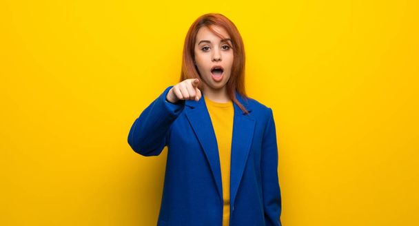 Young redhead woman with trench coat surprised and pointing front - Photo, Image