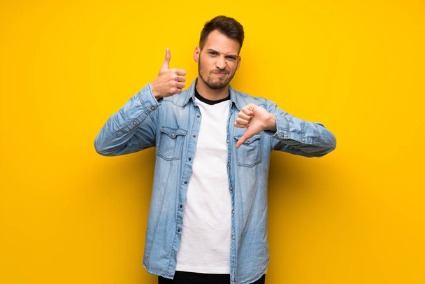 Handsome man over yellow wall making good-bad sign. Undecided between yes or not - Fotó, kép