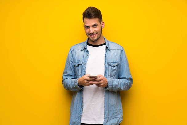 Красивый человек над желтой стеной отправляет сообщение с мобильным телефоном
 - Фото, изображение