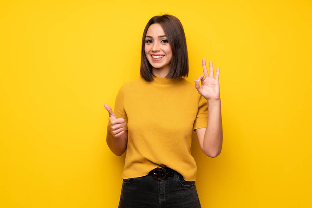 Jeune femme sur le mur jaune montrant ok signe avec et donnant un pouce geste
 - Photo, image