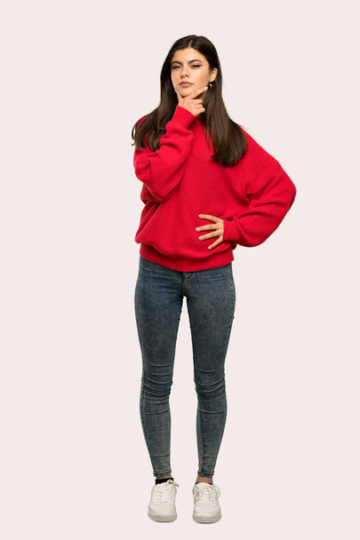 孤立した背景に赤いセーター思考とティーンエイ ジャーの女の子のフルレングス ショット - 写真・画像