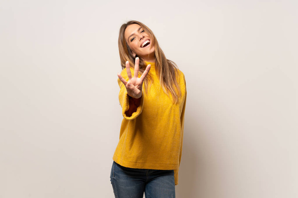 Frau mit gelbem Pullover über isolierter Wand glücklich und zählt mit den Fingern vier - Foto, Bild