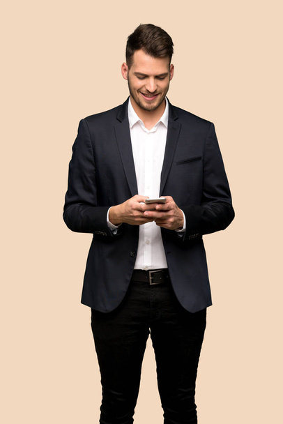 Όμορφος επιχείρηση άνθρωπος αποστέλλοντας ένα μήνυμα με το κινητό μέσω φόντο ώχρα - Φωτογραφία, εικόνα