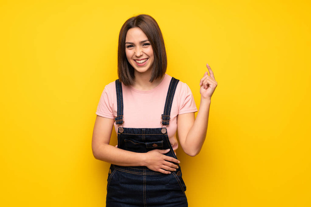 Jonge vrouw over gele muur glimlachend alot - Foto, afbeelding