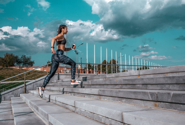 Young athletic girl running morning for jog, fitness training, sportswear, leggings and top. Phone listens music headphones. Summer city workout, online playlist application to Internet. Free space. - Valokuva, kuva