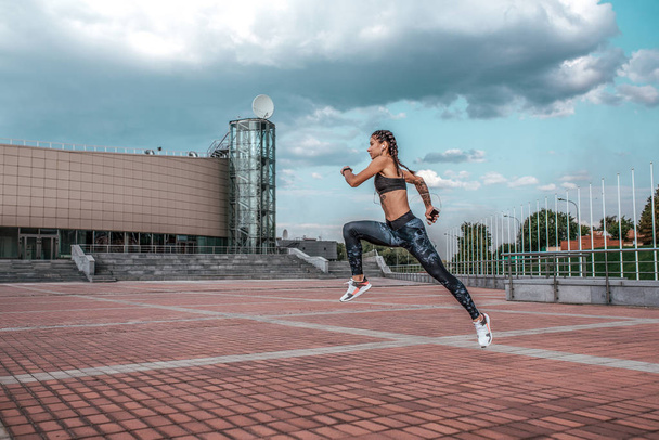 High jump. Young athletic girl running morning jog fitness training sportswear leggings and top. Phone listens music headphones. Summer city workout, online playlist application Internet. Free space. - Photo, Image