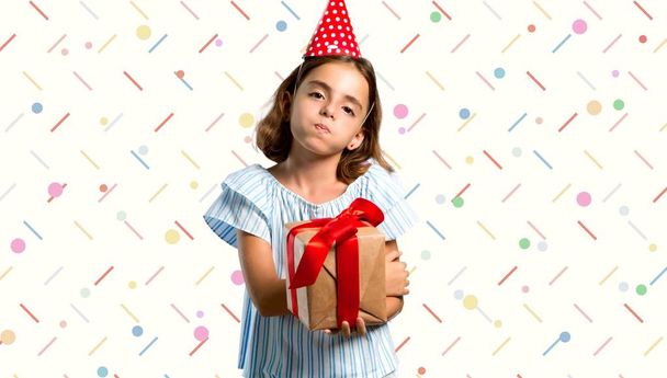 Niña en una fiesta de cumpleaños sosteniendo un regalo hace divertida y loca cara emoción sobre fondo colorido
 - Foto, imagen