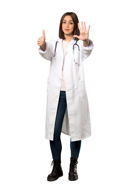 Een full-length schot van een jonge dokter vrouw tellen zes met vingers over geïsoleerde witte achtergrond - Foto, afbeelding