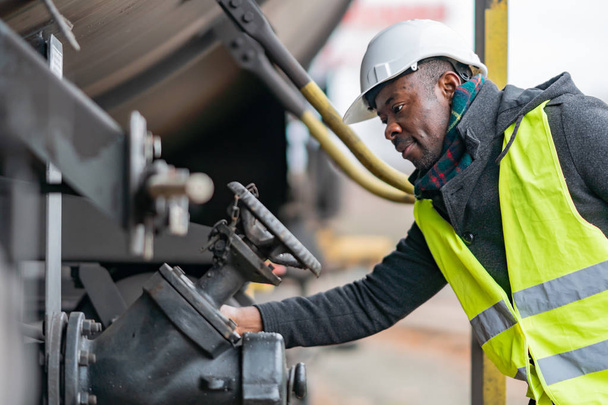 Meccanico afro-americano con equipaggiamento di sicurezza (casco e giacca) che controlla e ispeziona il treno di ingranaggi
 - Foto, immagini