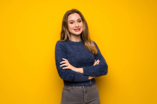 Teenager girl over yellow wall keeping the arms crossed in frontal position - Foto, afbeelding
