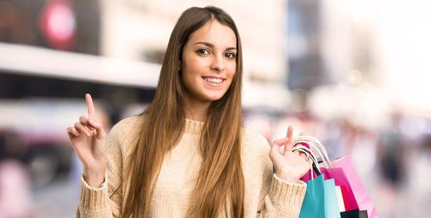 junges Mädchen mit Einkaufstaschen zeigt und hebt einen Finger im Zeichen des Besten in der Stadt - Foto, Bild