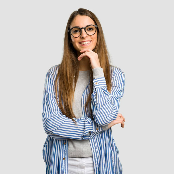 Молода дівчина з смугастою сорочкою в окулярах і посміхається над ізольованим сірим тлом
 - Фото, зображення