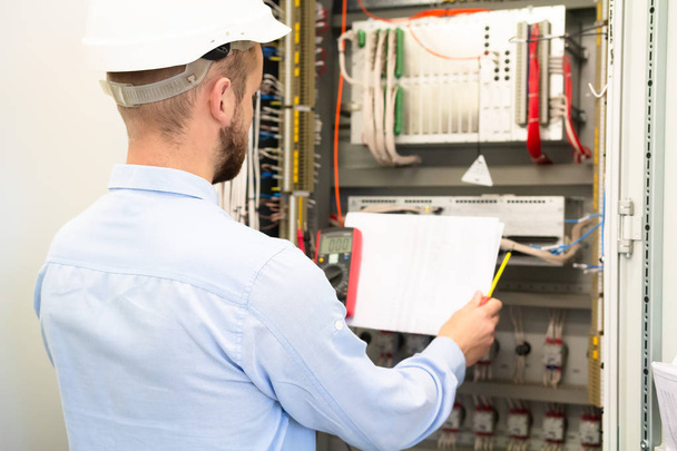Professional electrician in hardhat reads electric scheme near c - Foto, Imagem