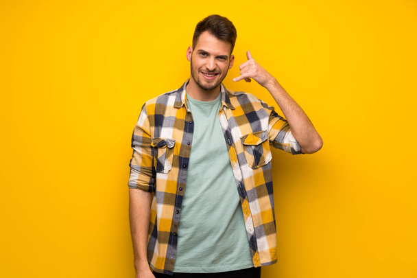 Hombre guapo sobre pared amarilla haciendo gesto de teléfono y dudando
 - Foto, Imagen