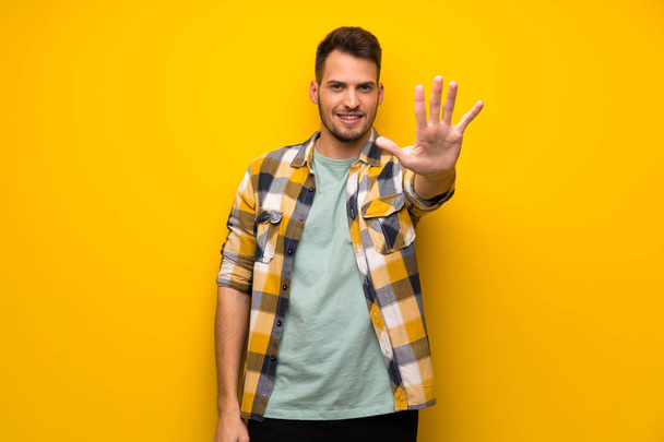 Beş parmak ile sayma sarı duvarın üzerinden yakışıklı adam - Fotoğraf, Görsel