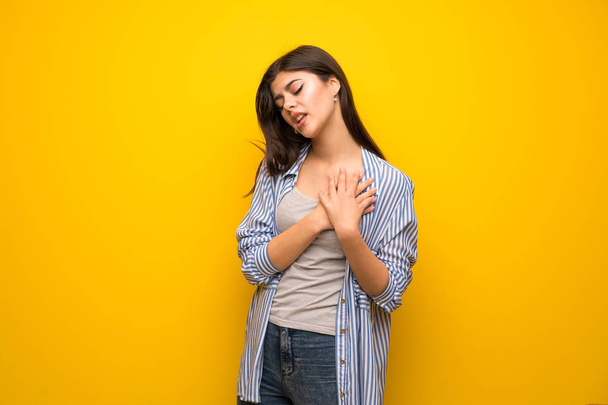 Teenager girl over yellow wall having a pain in the heart - Photo, Image