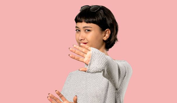Mladá žena s krátkými vlasy, nervózní a vystrašený, natahovat ruce dopředu na izolované růžové pozadí - Fotografie, Obrázek