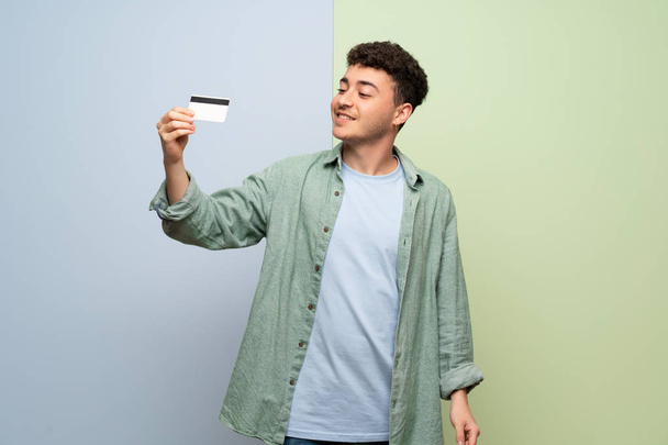 Nuori mies yli sininen ja vihreä tausta tilalla luottokortti ja ajattelu
 - Valokuva, kuva