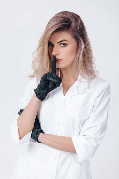 cosmetologist in black gloves shows sign silence. Woman beautician doctor - Foto, imagen
