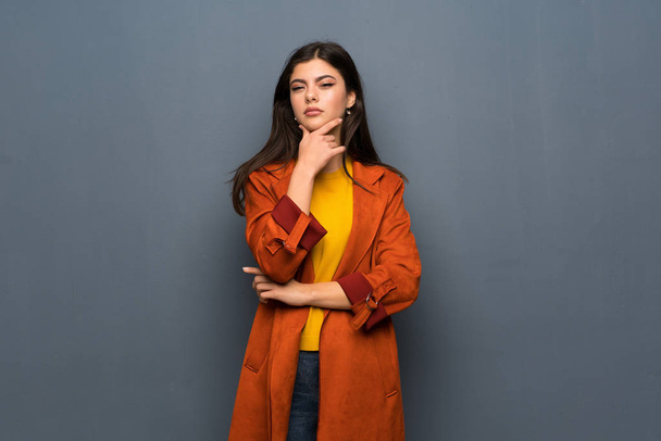 Teenager girl with coat over grey wall thinking - Valokuva, kuva