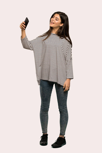 ストライプのシャツ、selfie をかけて孤立した背景とティーンエイ ジャーの女の子のフルレングス ショット - 写真・画像