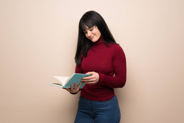 Jeune femme au col roulé rouge tenant un livre et appréciant la lecture
 - Photo, image