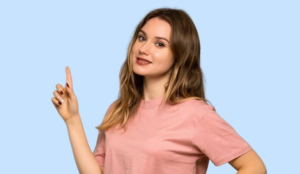 Tiener meisje met roze trui tonen en een vinger in teken van het beste op geïsoleerde blauwe achtergrond - Foto, afbeelding