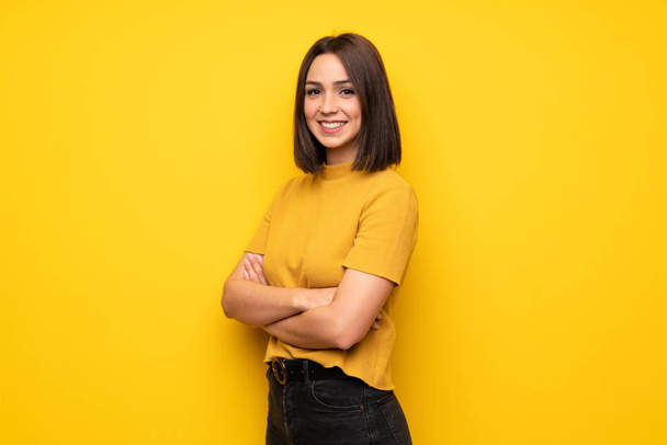 Jovem mulher sobre a parede amarela com os braços cruzados e olhando para frente
 - Foto, Imagem