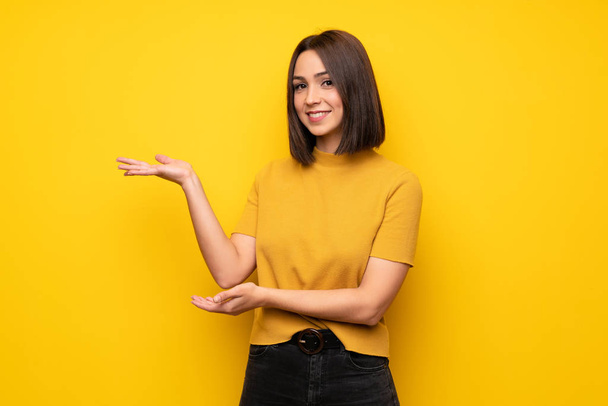 Young woman over yellow wall extending hands to the side for inviting to come - Photo, Image