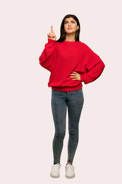 Ένα ολόσωμο πλάνο ενός εφήβου κορίτσι με κόκκινο πουλόβερ με δάχτυλα διέλευση και επιθυμούν το καλύτερο πέρα από το απομονωμένο υπόβαθρο - Φωτογραφία, εικόνα