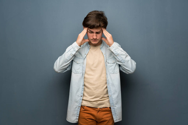 Adolescente homem com jaqueta de jeans sobre parede cinza com dor de cabeça
 - Foto, Imagem