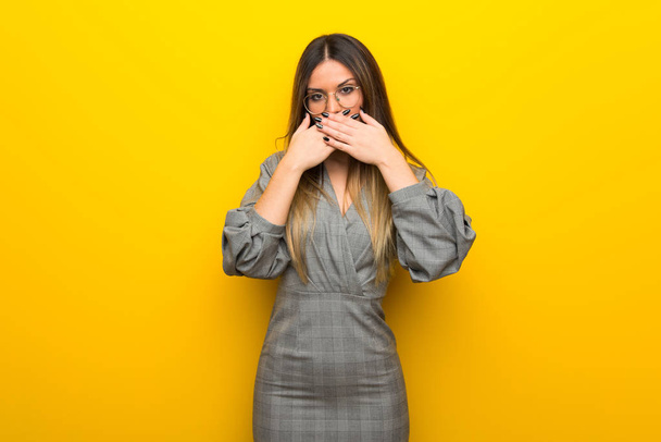 junge Frau mit Brille über gelber Wand, die Mund mit Händen bedeckt, weil sie etwas Unpassendes sagt - Foto, Bild