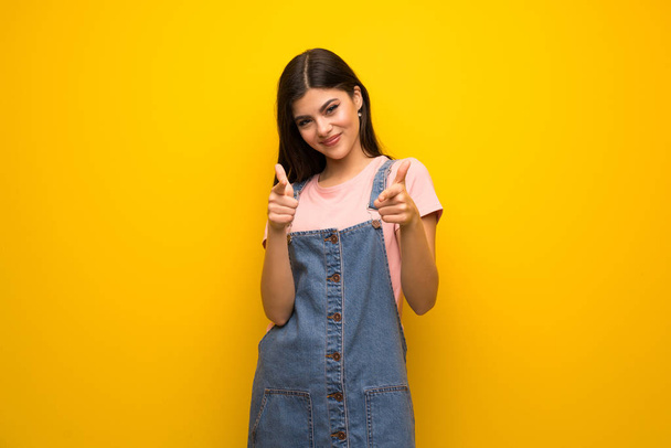 Teini tyttö yli keltainen seinä osoittaa eteen ja hymyilee
 - Valokuva, kuva