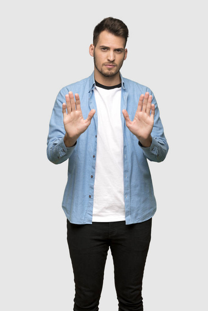 Handsome man making stop gesture and disappointed over grey background - 写真・画像