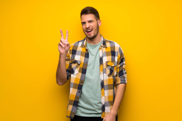 schöner Mann über gelber Wand lächelt und zeigt Siegeszeichen - Foto, Bild