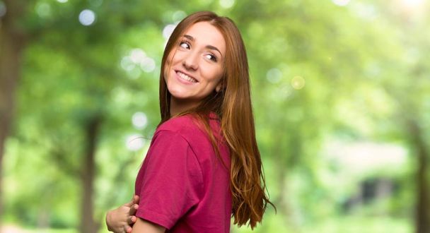 Jonge roodharige meisje kijken over de schouder met een glimlach in het park - Foto, afbeelding
