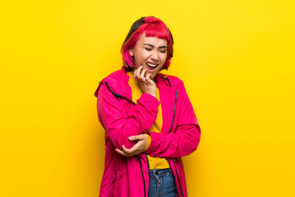 Jonge vrouw met roze haren over gele muur met kiespijn - Foto, afbeelding