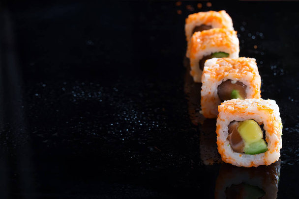 California Maki Sushi with Masago - Roll made of Crab Meat, Avocado, Cucumber on glass black background, copy space - Photo, Image