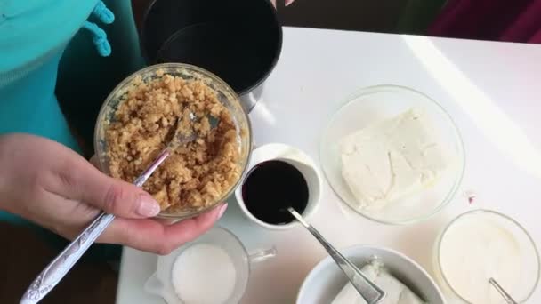 A woman pours crumb biscuits with butter in the form for cheesecake. - Filmmaterial, Video